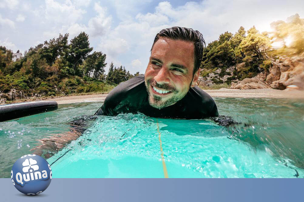 Homem feliz surfando na praia e curtindo a aposentadoria precoce ao ganhar com as dicas da Quina