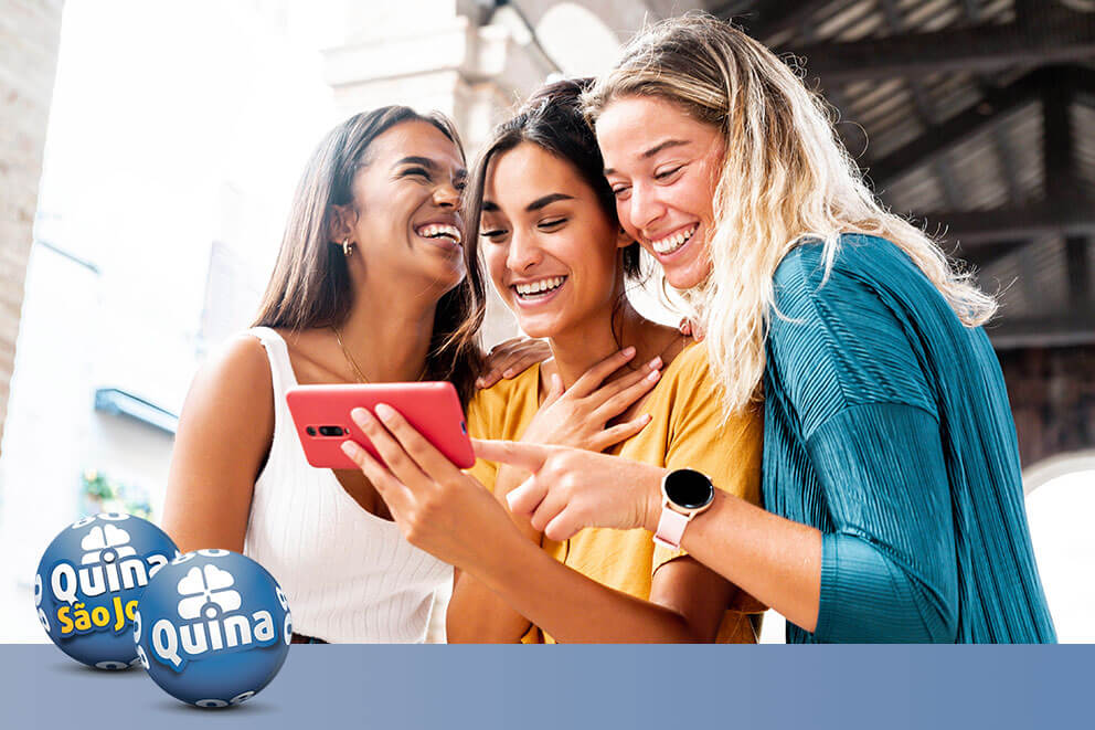 Três amigas sorrindo ao olhar suas apostas ganhadoras no bolão da Quina e Quina de São João.
