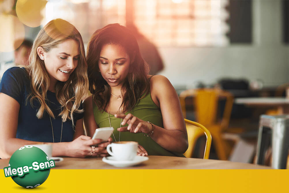 Duas mulheres sentadas numa cafeteria conferindo os resultados da Mega Sena online.