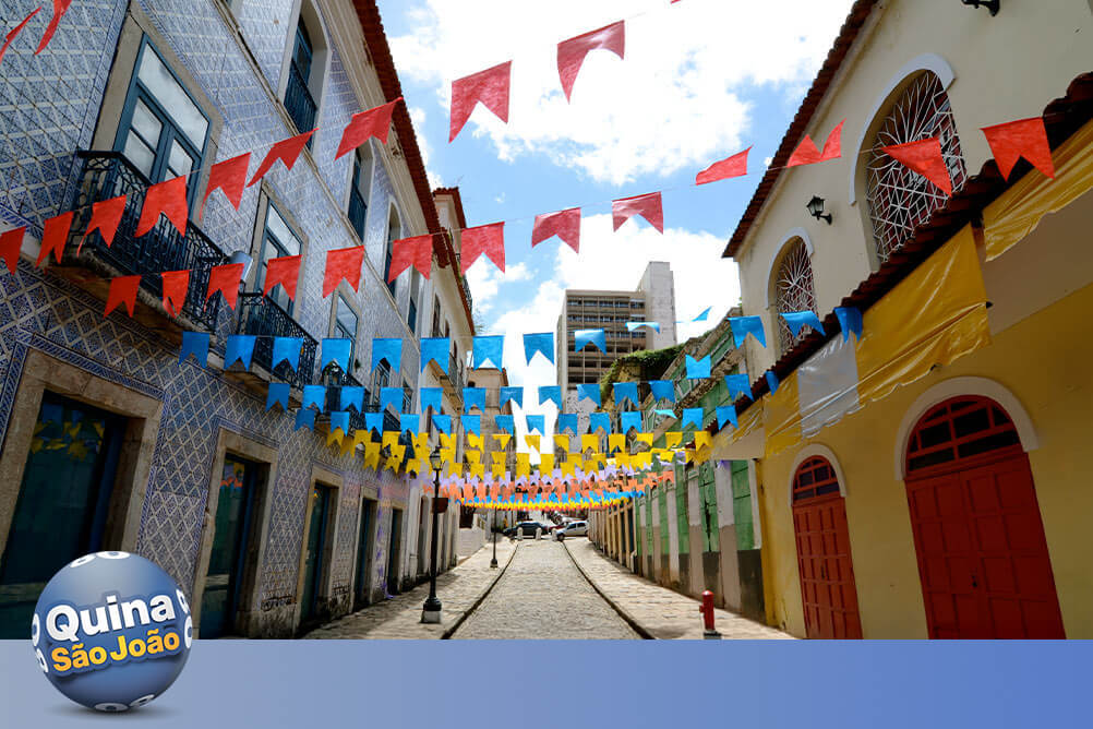 Imagem de uma rua decorada com bandeirolas juninas, casas coloridas e uma casa de apostas que ensina como jogar na Quina de São João.