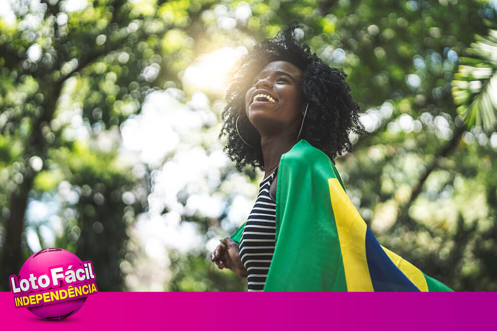 Mulher sorrindo com bandeira do Brasil, fazendo uma aposta na Lotofácil da Independência para celebrar a data nacional.