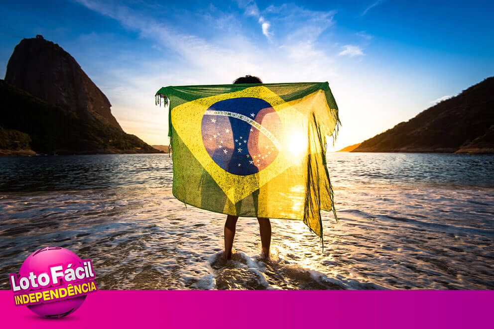 Como jogar Lotofácil da Independência 2025 Pessoa na praia usando a bandeira do Brasil em homenagem à Independência do Brasil, descansando depois de fazer apostas na Lotofácil da Independência 2025 online.